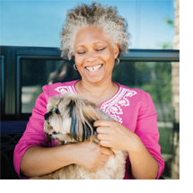 Photo: Mature woman smiling while holding and petting her dog.