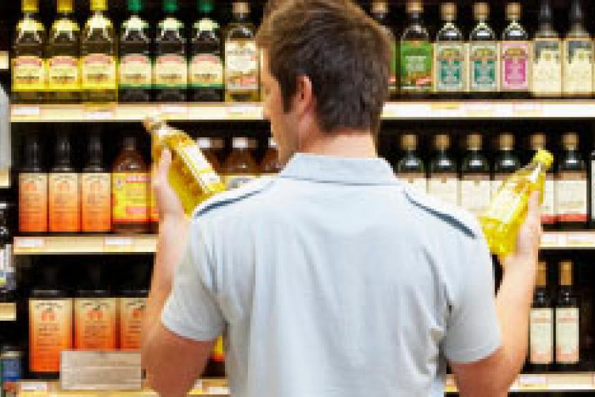 Photo: Man looking at two bottles of olive oil in supermarket aisle
