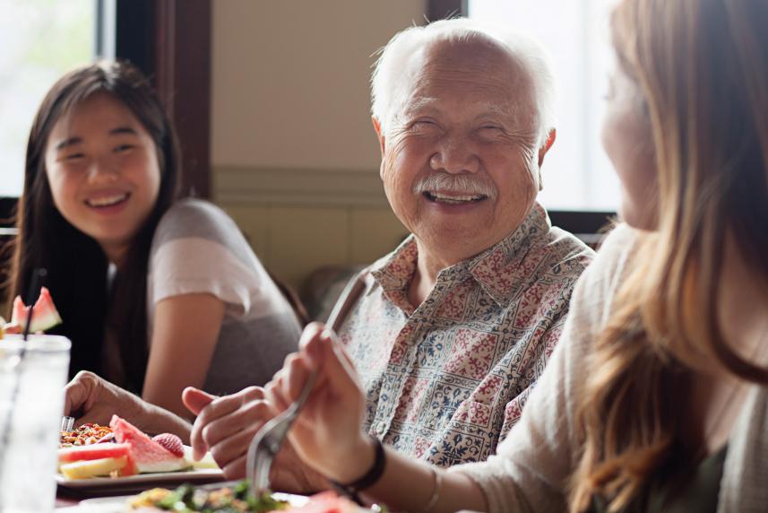 Photo: Elderly man smiling at dinner table with two granddaughters.
