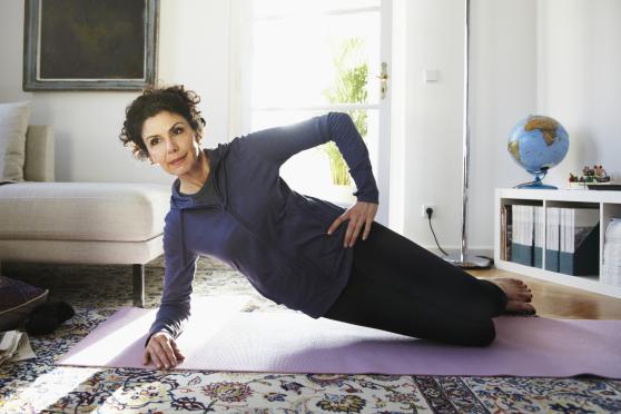 A woman in a purple hoodie does yoga on a purple yoga mat in a living room.