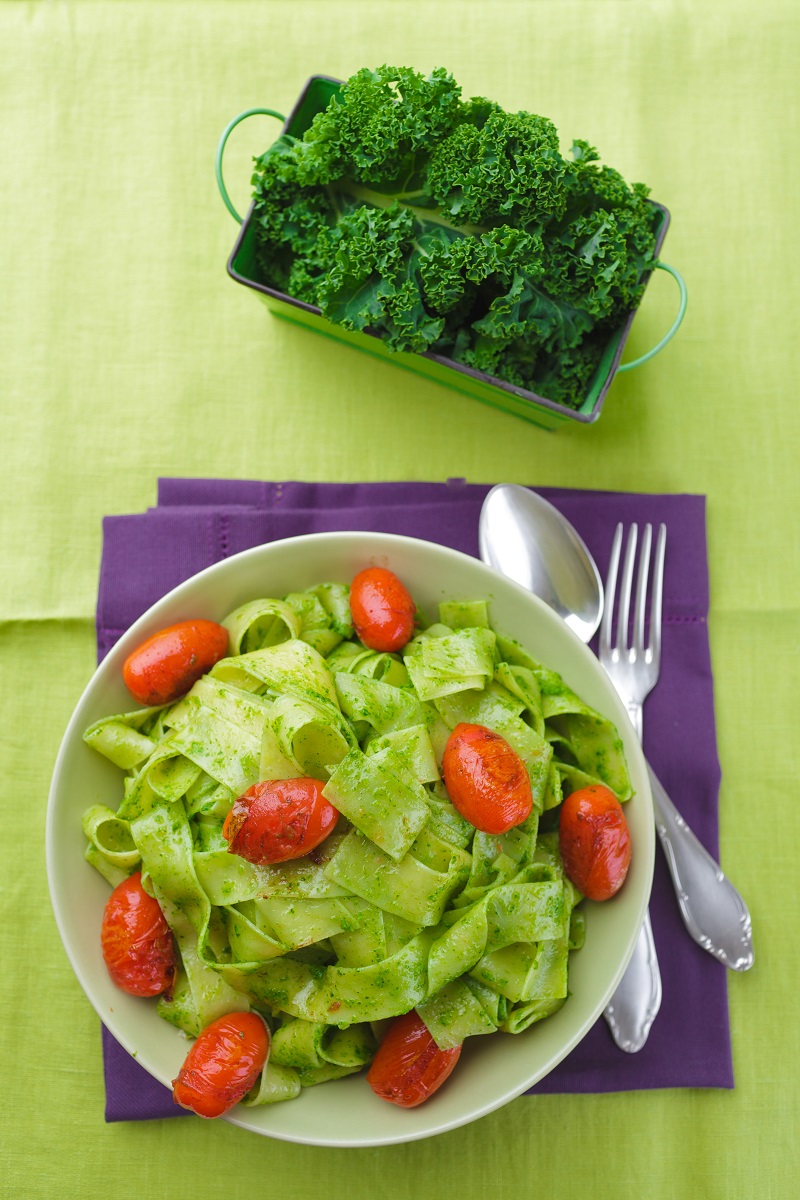 Bowl of kale pesto pasta salad, on a napkin with a fork and spoon.