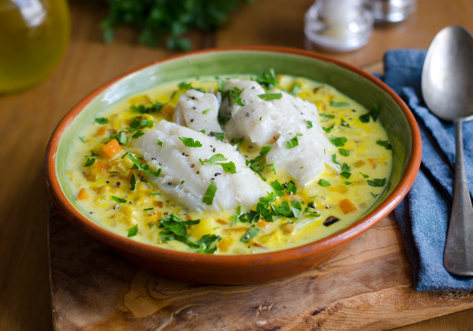 Photo: Bowl of creamy fish and chive chowder, with rustic table setting.