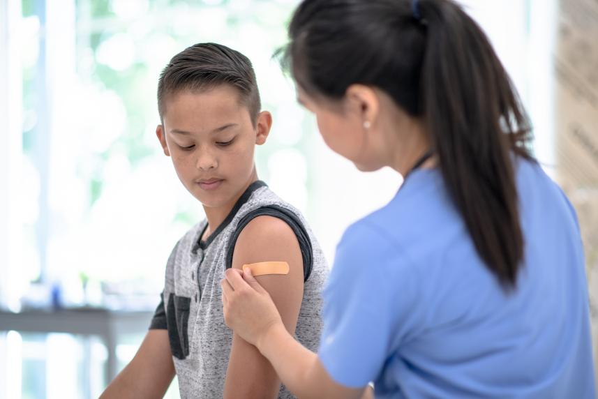 A nurse places a bandage on a young boy's upper arm, where he just received a vaccination.