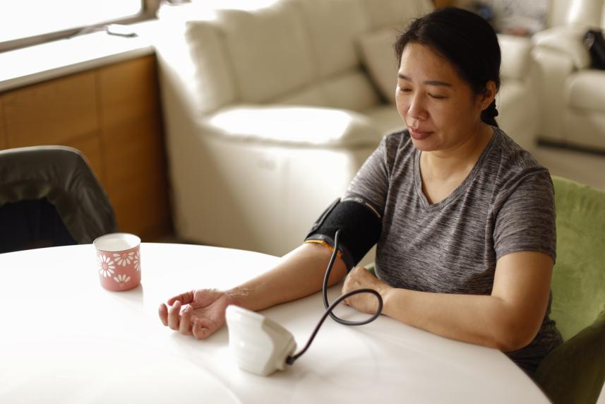 A woman takes her blood pressure at a table in her home.