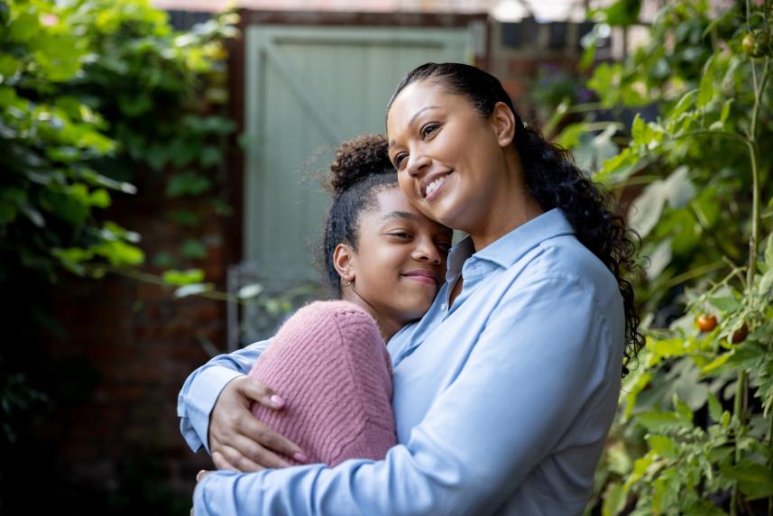 A smiling mother embraces her daughter outside their home.