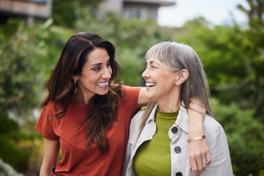 A brunette woman laughs with her shoulder hooked around her mother's, who had gray hair and bangs.