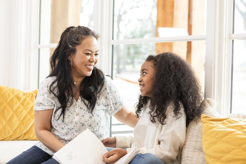 A mother and daughter smile as they flip through the pages of a book together.