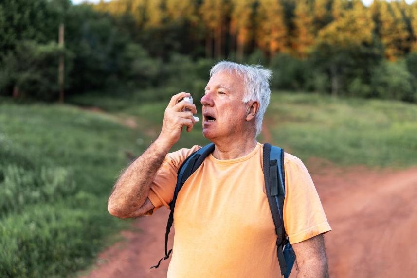 An older man uses his rescue inhaler while on a walk outdoors