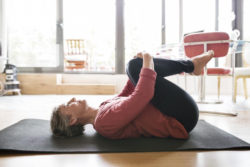 A woman stretches her lower back on a yoga mat.