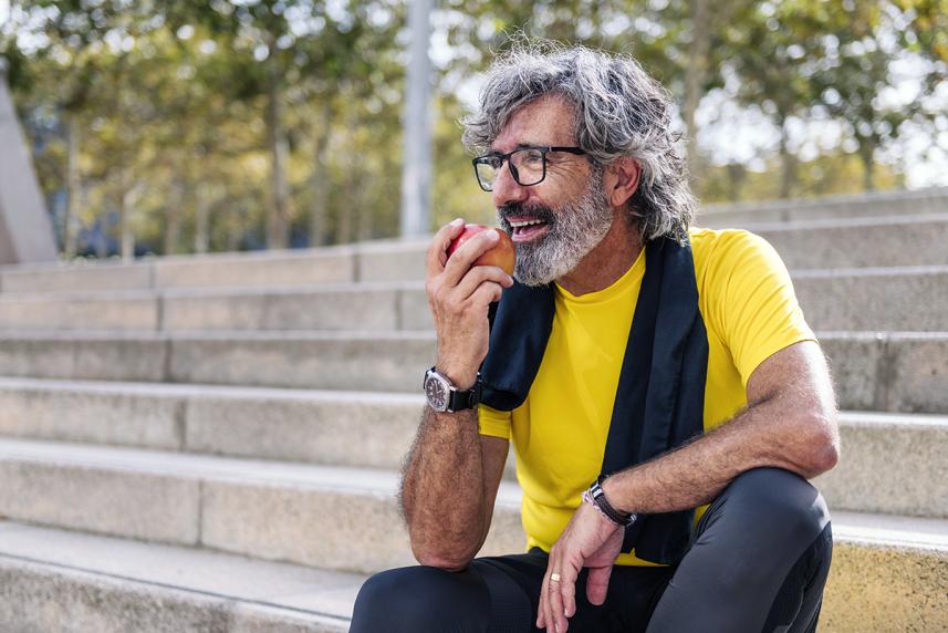 Mature man eating an apple outside, sitting on steps