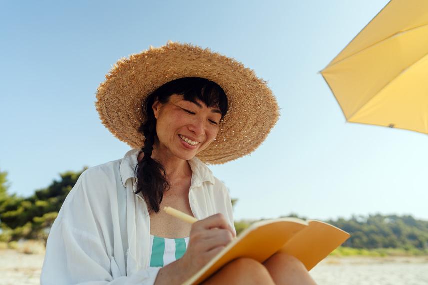 Woman smiling sitting on the beach journaling.