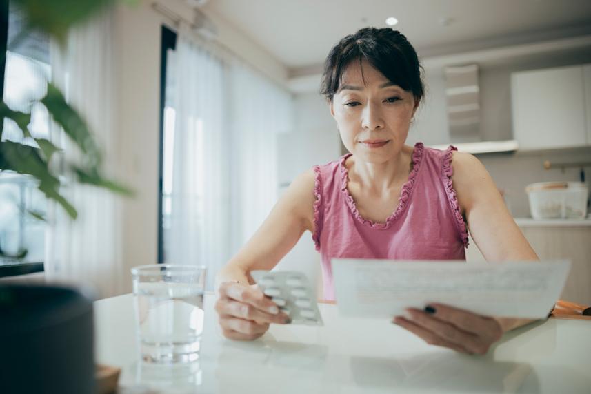 A middle-aged Asian woman in a pink tank top blouse reviews her medications.