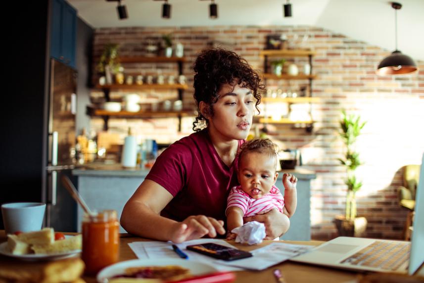 Woman holding baby using a laptop at a cafe.