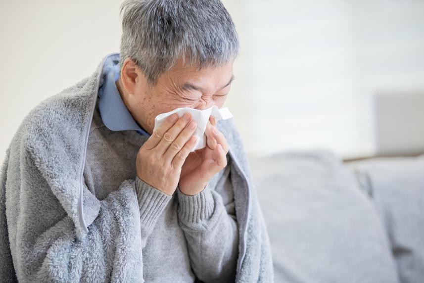 Man blowing his nose into a tissue while wearing a blanket