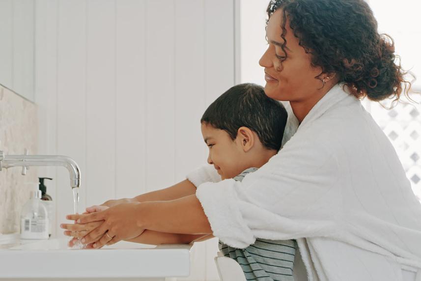 A mother helping her child wash thier hands.