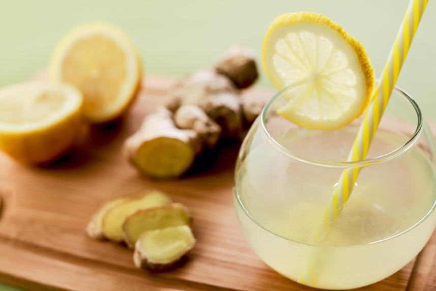 Pitcher with lemonade and yellow straw on a cutting board with a piece of raw ginger and a lemon cut in half