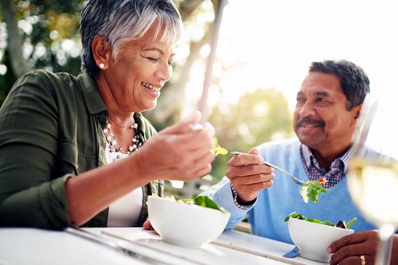 Mature couple smiling and eating salad outdoors