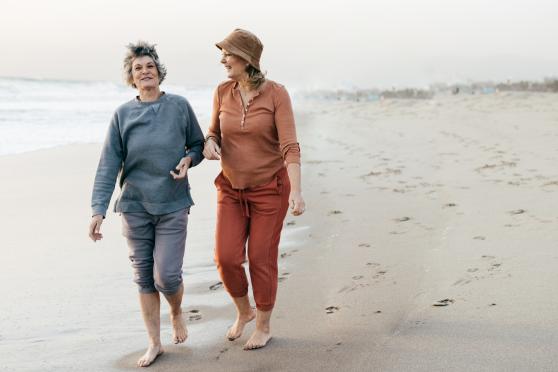 Two women are happily chatting with each other as they walk barefoot along the shoreline of an empty beach.