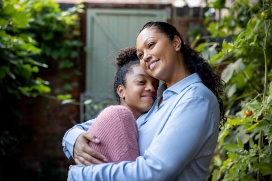 A smiling mother embraces her daughter outside their home.