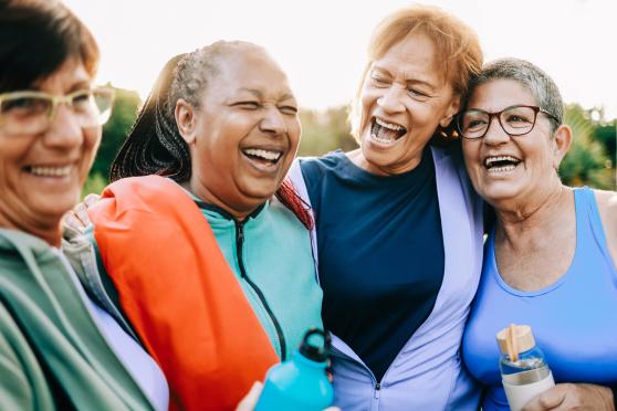 Four women laugh together during an group hug after their outdoor workout together.