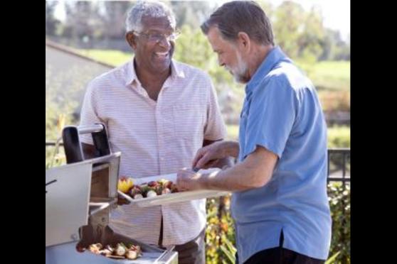 A man talking to a friend getting food off a grill