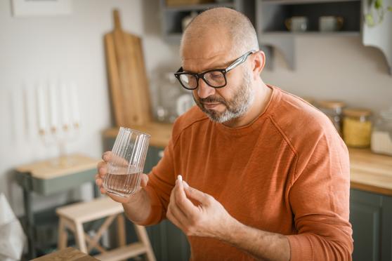 A man examines a pill while he holds a glass of water, preparing to take his medication.