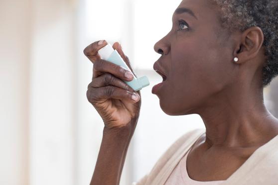 A Black woman in a white sweater uses a rescue inhaler.