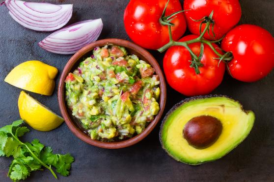 Guacamole and ingredients - avocado, tomatoes, onion, cilantro dark background