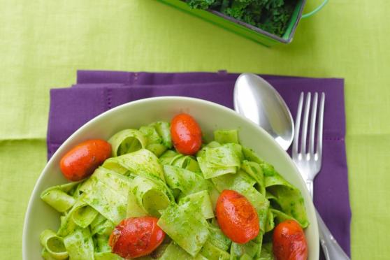 Bowl of kale pesto pasta salad, on a napkin with a fork and spoon.