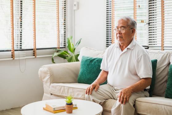 A man sitting upright on a couch, eyes closed