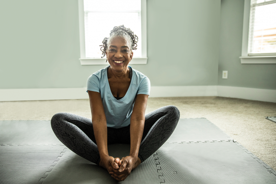 African American woman sitting on floor stretching & smiling