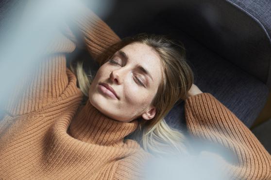 Portrait of woman relaxing on the couch arms with eyes closed and arms behind her head.