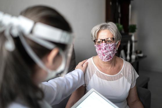 Senior patient woman being comforted by doctor, both wearing masks.