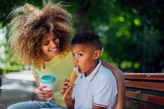 A mother and son enjoy a sweet treat on a local park bench. 