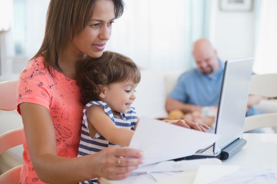 Photo: Woman working on computer with child on lap.